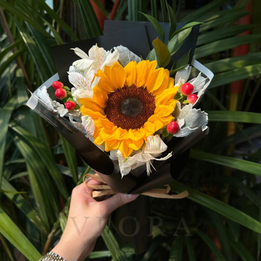 Bouquet with a sunflower held by a hand against a green leafy background