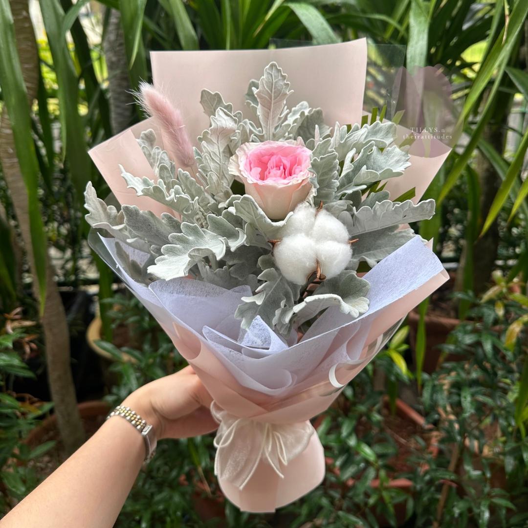 Bouquet of flowers with pink carnation and cotton held by a person against a green foliage background