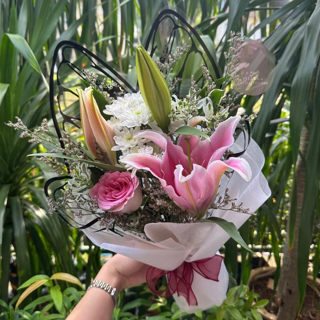 Bouquet of pink flowers with a butterfly-shaped holder held by a person against a green leafy background.