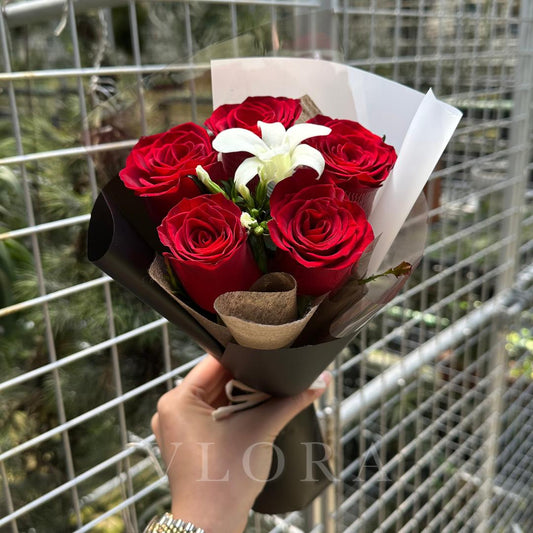 Bouquet of red roses with a white flower held by a hand against a wire fence background.