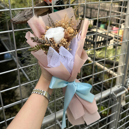 Bouquet of flowers held by a person in front of a wire fence with plants in the background