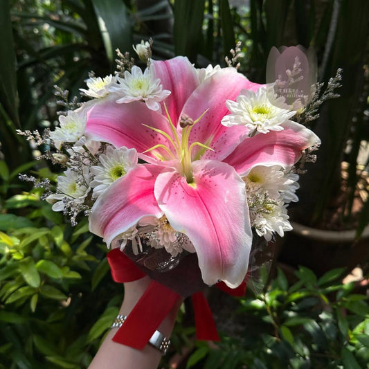 Bouquet of pink and white flowers held by a person with greenery in the background