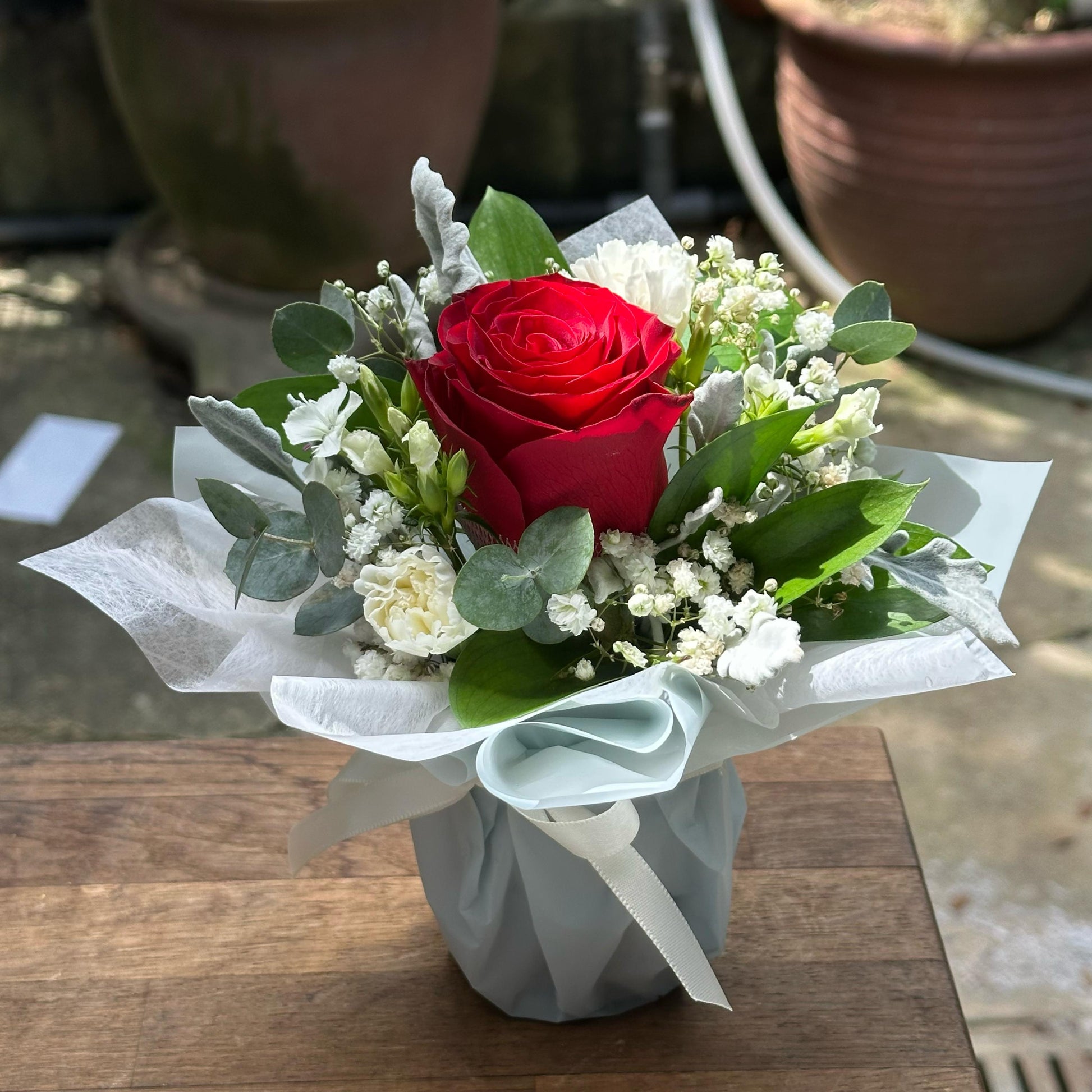 Bouquet with a red rose and greenery on a wooden surface