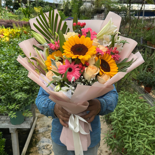 a large Bouquet of flowers with sunflowers and pink flowers held by a person in a garden setting.