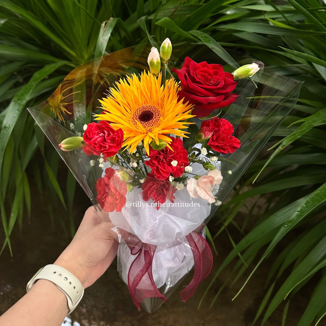 Bouquet of red and yellow flowers held by a person with green foliage in the background