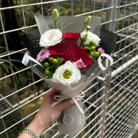 Bouquet of red, white, and pink flowers held by a hand with a blurred background