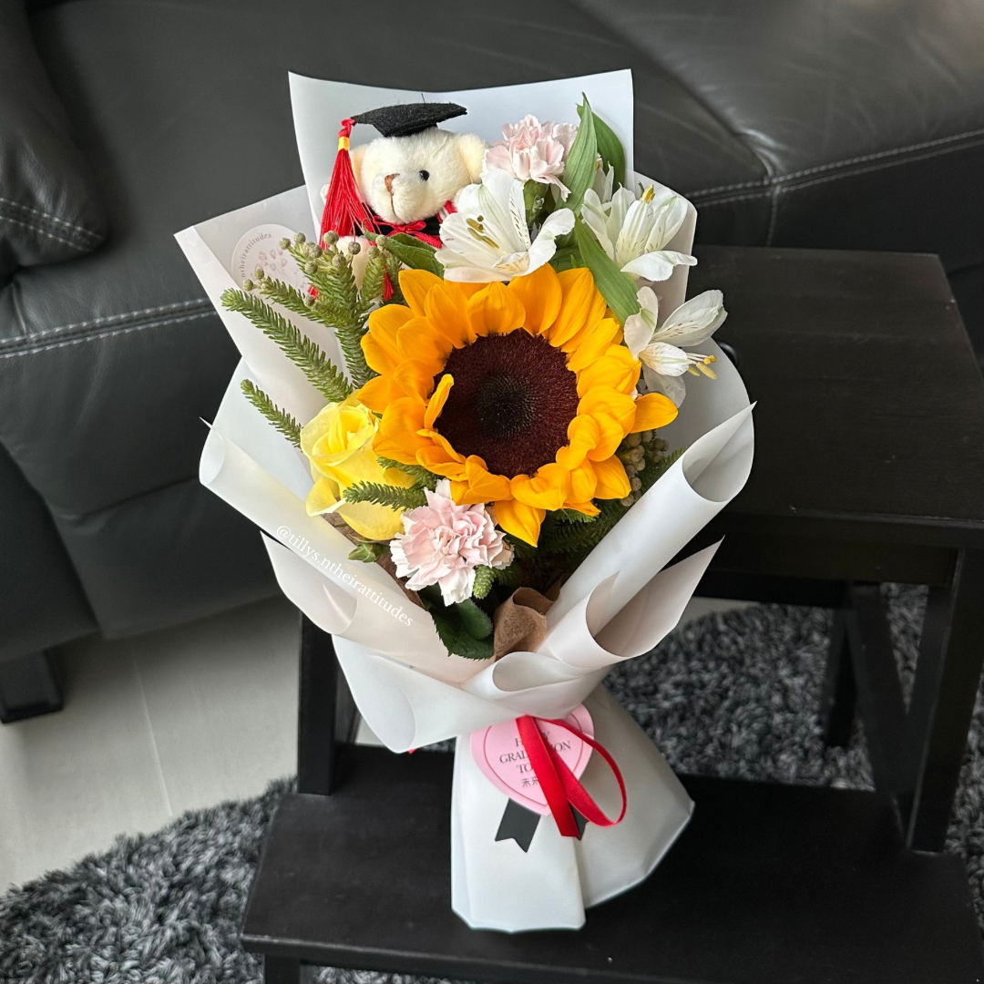 A sunflower graduation bouquet with a graduation bear wrapped in white.