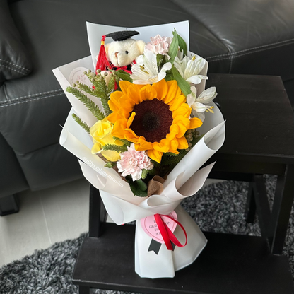 A sunflower graduation bouquet with a graduation bear wrapped in white.