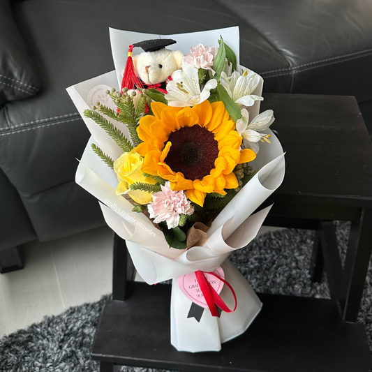A sunflower graduation bouquet with a graduation bear wrapped in white.