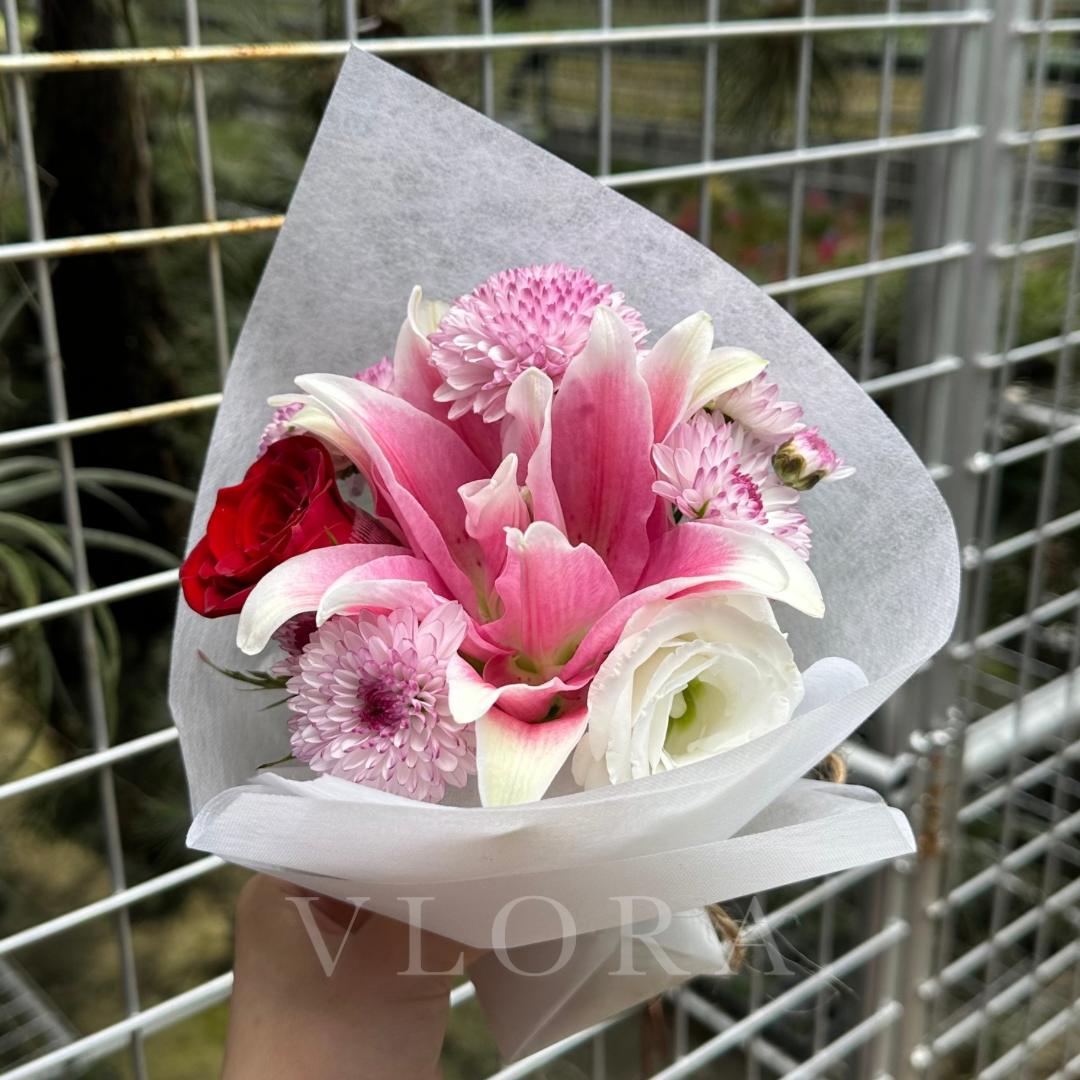 Bouquet of pink and white flowers wrapped in gray paper held against a wire fence.