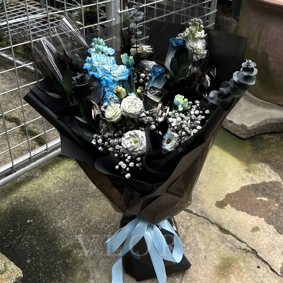 Bouquet of black flowers wrapped in black paper with a blue ribbon on a concrete surface.