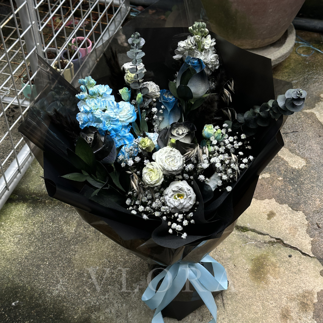 Bouquet of black and blue flowers wrapped in black paper with a blue ribbon on a platform.