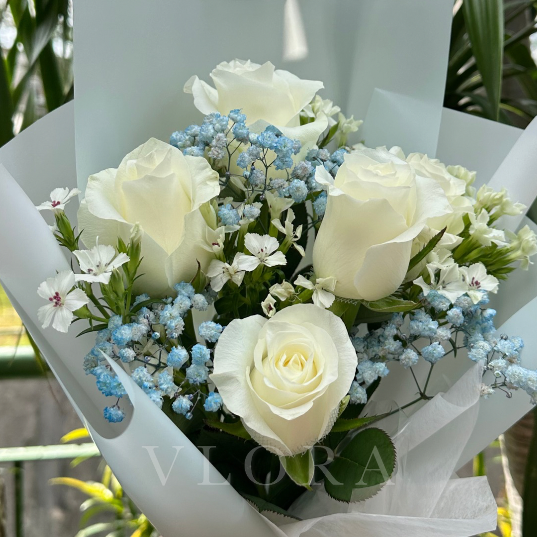 Bouquet of white roses with small blue baby's breath, white baby's breath, and greenery, wrapped in white paper.
