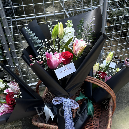 Bouquet of flowers with a black wrap and visible 'Vlora' branding in a wicker basket.